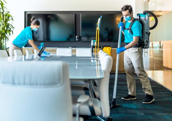 Two ServiceMaster Clean janitors vacuuming the floor and wiping down a table in a office conference room